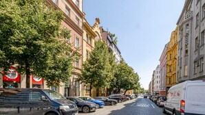 En kullerstensgata kantad av parkerade bilar och träd, med byggnader som uppvisar klassisk arkitektur och butiksfasader med väl synliga skyltar.