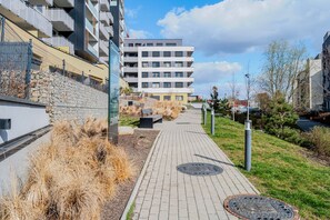 A pathway leading to a modern building with multiple floors, a stone wall, and a grassy area with benches. - Blueground | Michle, Prague 4, nr Vysehrad (PRG-99) (Prague)