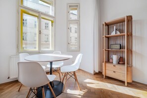 Ein Zimmer mit einem runden Tisch, weißen Stühlen, einem Holzregal und großen Fenstern.