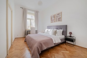 Ein Schlafzimmer mit Bett, Stuhl, Nachttisch und einem Fenster mit Vorhängen.