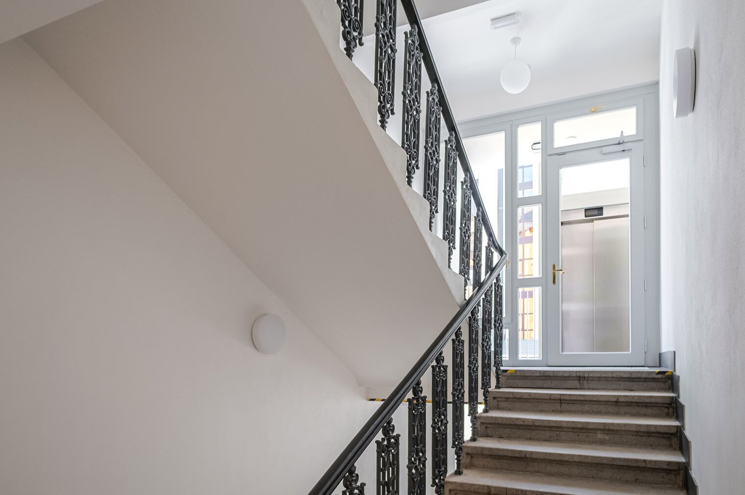 A staircase with ornate black railings leading to a door with a glass panel.