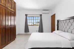 Ein Schlafzimmer mit Bett, Kleiderschrank, einem Fenster mit Vorhängen und einer Klimaanlage.