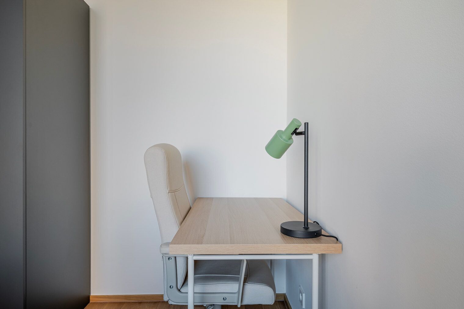 A corner desk with a chair, a green desk lamp, and a light-colored table.