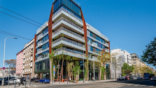 Um edifício moderno de vários andares com um design angular peculiar, grandes janelas e um jardim no terraço.