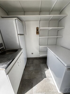 Una cocina compacta con electrodomésticos blancos, un lavamanos de acero inoxidable y una estantería empotrada.