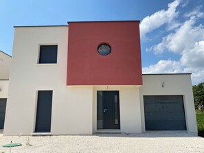 Un bâtiment moderne à deux étages, doté d’un mur d’accent rouge, d’un garage et d’une petite fenêtre.