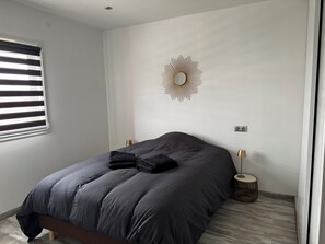 Ein Schlafzimmer mit einem Bett, einem wandmontierten Spiegel, Nachttischlampen und einem Fenster mit Jalousien.