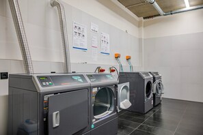 A laundry facility with multiple washing machines and dryers, ventilation ducts, and informational posters on the wall. - Blueground | Smíchov, rooftop, nr Vltava River (PRG-106) (Prague)