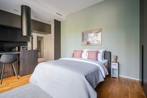 Un dormitorio moderno con una cama grande, un escritorio pequeño y una kitchenette al fondo.