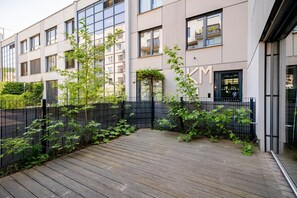 A modern building with a wooden deck, a black metal fence, and greenery. - Blueground | Smíchov, rooftop, nr Vltava River (PRG-106) (Prague)