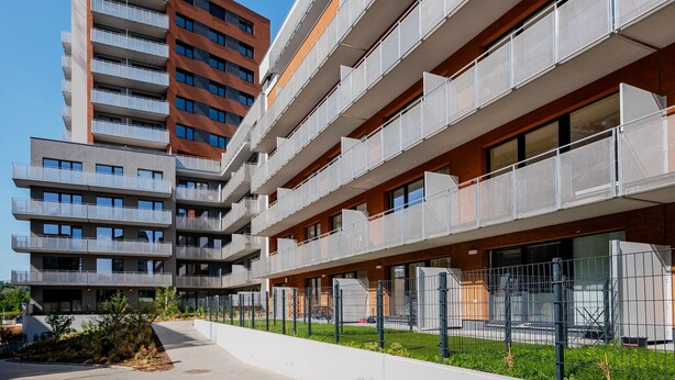 Un edificio de varios pisos con balcones, cielo despejado y un camino pavimentado.