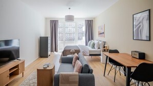 Una habitación de hotel moderna con televisión de pantalla plana, sofá, cama, escritorio y un amplio ventanal.