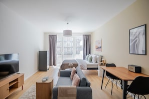 Ein modernes Hotelzimmer mit Flachbildfernseher, einer Couch, einem Bett, einem Schreibtisch und einem großen Fenster.