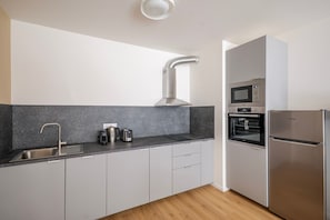 Eine moderne Küche mit Spüle aus Edelstahl, Wasserkocher, Toaster, Backofen und Kühlschrank.