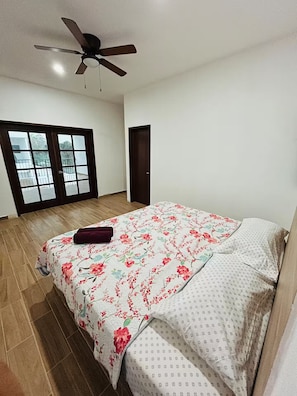 Une chambre à coucher avec un lit, un ventilateur de plafond, une fenêtre donnant sur un paysage agréable et une porte.