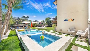 Ein Swimmingpool mit Liegestühlen, einer Surfbrett-Dekoration und einem gepflegten Rasen.