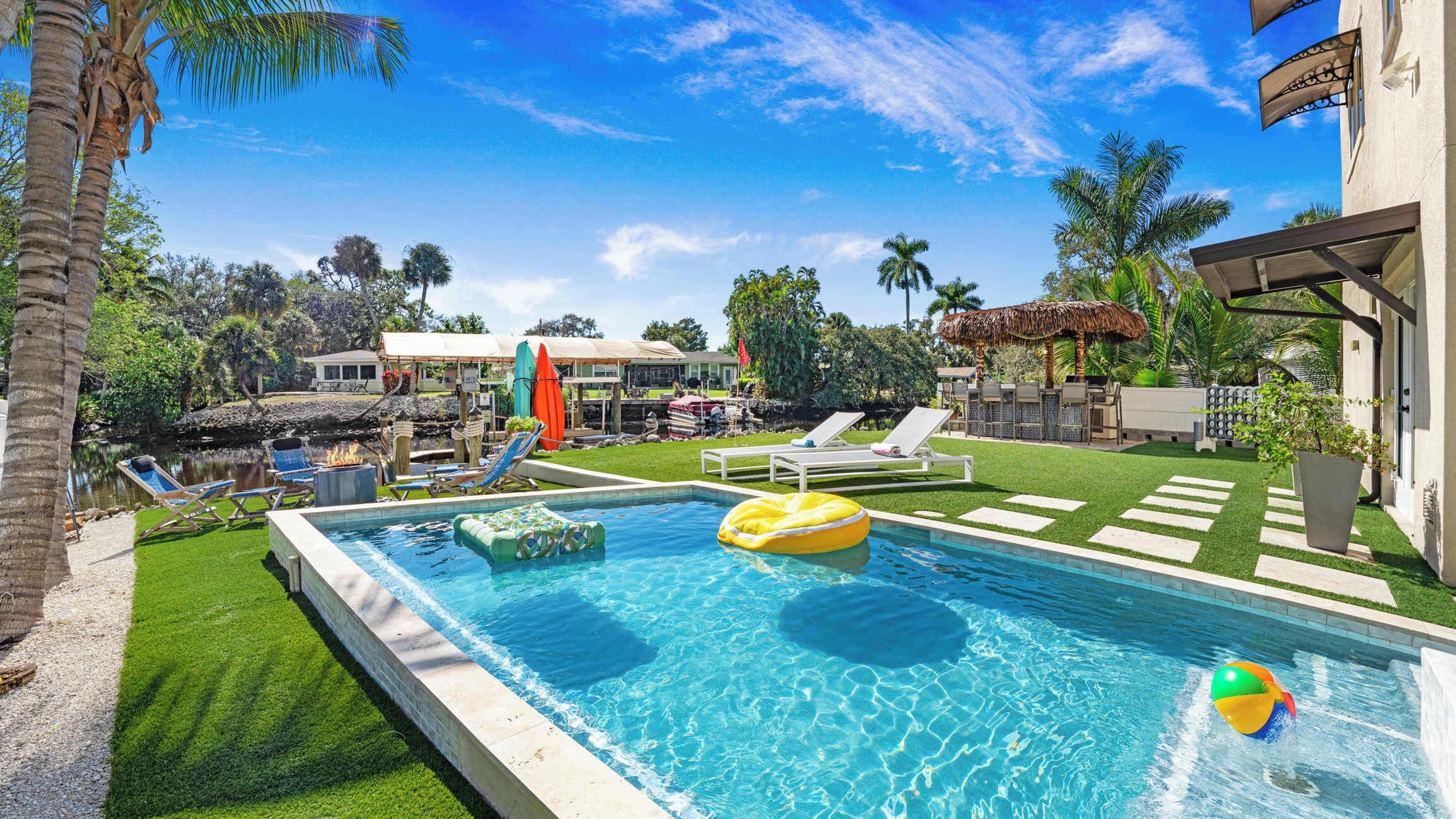 A swimming pool with lounge chairs, a thatched umbrella, and a tiki hut.
