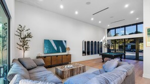 A modern living room with a pool table, a large sofa, a wooden coffee table, and a television on the wall. - 4BR Sleek, Art, Design District, Private Pool, Ping Pong & Grill (Miami)