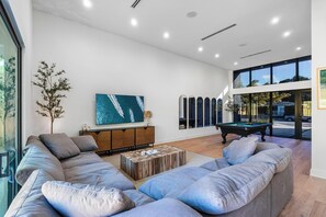 A modern living room with a pool table, a large sofa, a wooden coffee table, and a television on the wall. - 4BR Sleek, Art, Design District, Private Pool, Ping Pong & Grill (Miami)