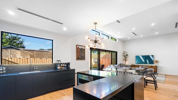 A modern kitchen with a black countertop, wooden flooring, and a dining area with a glass table and chairs. - 4BR Sleek, Art, Design District, Private Pool, Ping Pong & Grill (Miami)