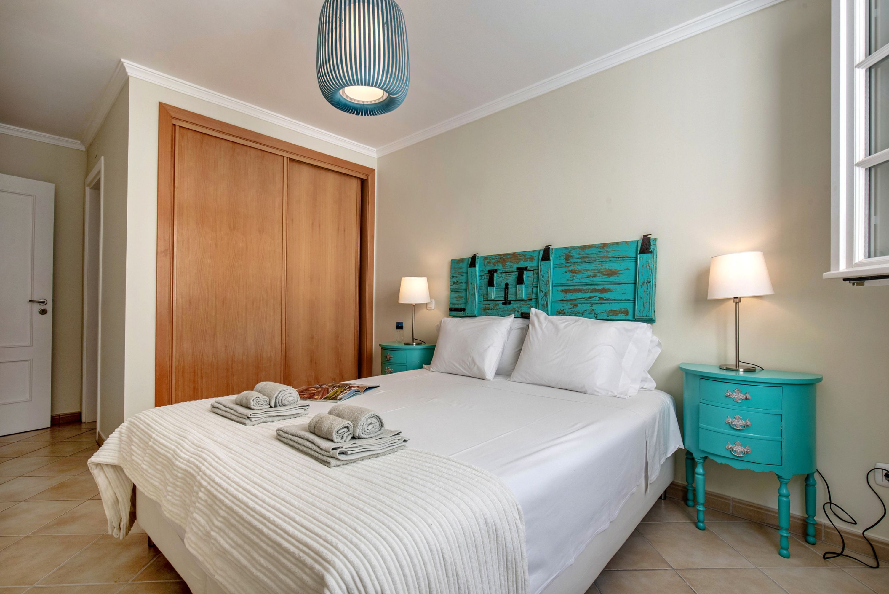Une chambre à coucher avec un lit, deux tables de chevet, une armoire en bois et une fenêtre.