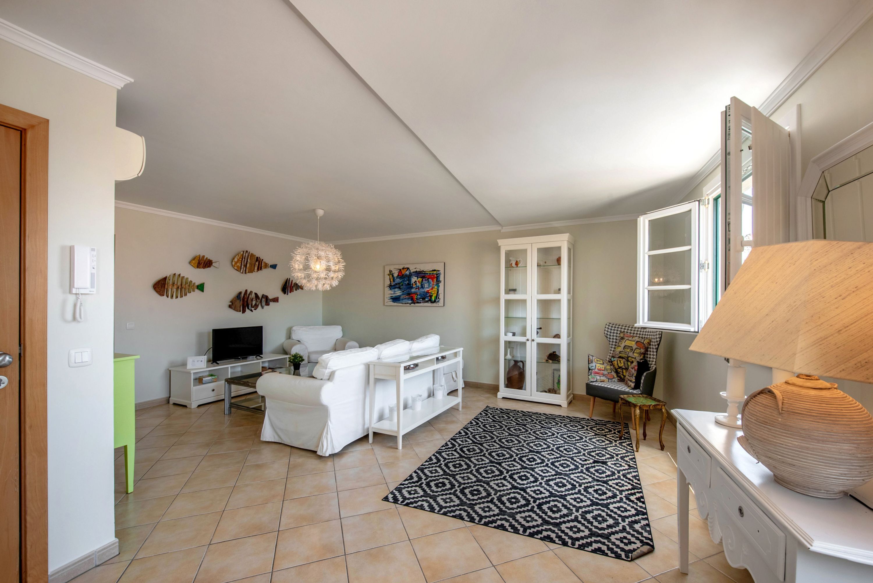 Una sala de estar con un sofá, televisor, decoración en la pared, un tapete estampado y un mueble.