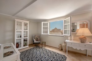 Ein Zimmer mit einem weißen Schrank, einem Stuhl, einem Fenster mit Ausblick, einer Lampe und einem gemusterten Teppich.