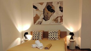 Una habitación de hotel con una cama grande, dos lámparas de noche, un cuadro en la pared y suelo de madera.