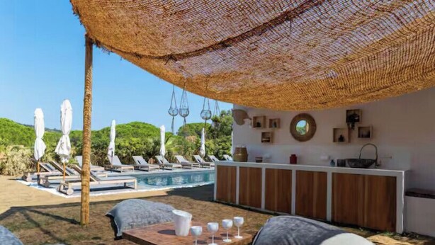 Un espace aménagé au bord de la piscine, avec des chaises longues, une table en bois avec des verres et un bar doté de meubles en bois.