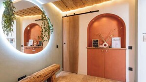 Un espace d’accueil comprenant un banc en bois, un miroir rond, un comptoir d’accueil et une porte en bois avec une enseigne.