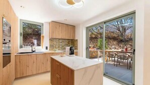 Une cuisine moderne avec des meubles en bois, un plan de travail en marbre et une grande porte-fenêtre coulissante donnant sur un espace repas extérieur.