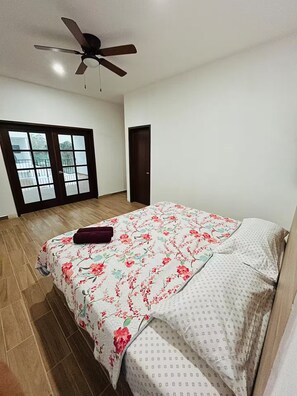 Een slaapkamer met een bed, een plafondventilator, een raam met uitzicht en een deur.