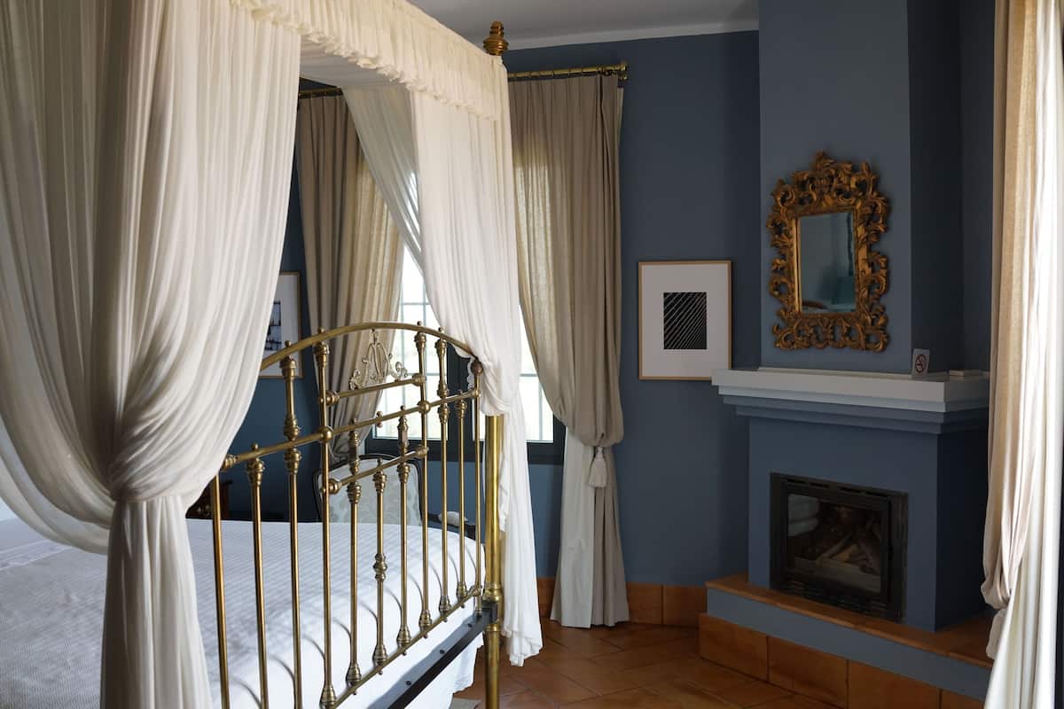 A bedroom with a four-poster bed, a fireplace, and a mirror on the wall.