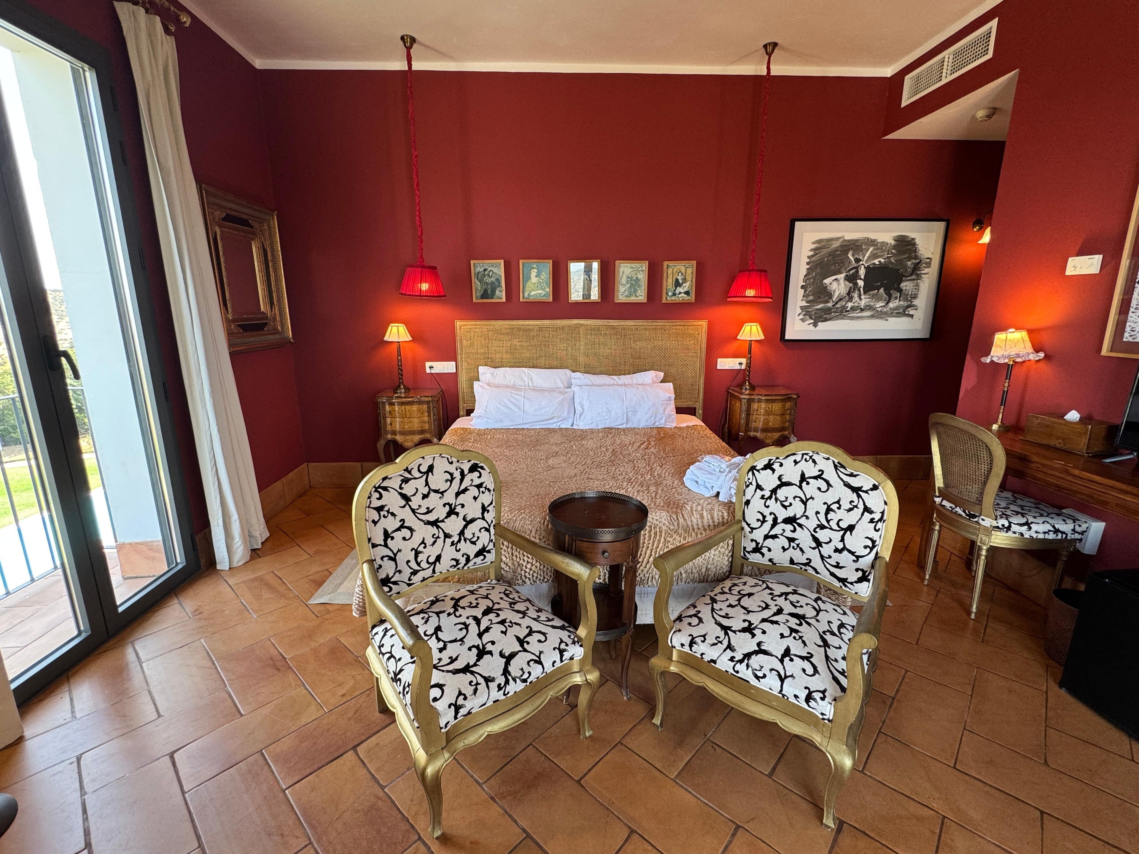 Una habitación de hotel con una cama, dos sillas, una mesita y un ventanal.
