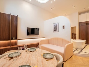 Ein modernes Wohnzimmer mit Fernseher, einem Esstisch gedeckt mit Tellern und Gläsern, einer Couch und einer Badewanne.
