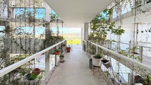 Un couloir bordé de plantes en pot de chaque côté, une rambarde blanche et une vue à travers les murs de verre.