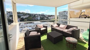 Un balcon agrémenté de meubles en osier, d’un gazon synthétique vert et offrant une vue sur la ville.