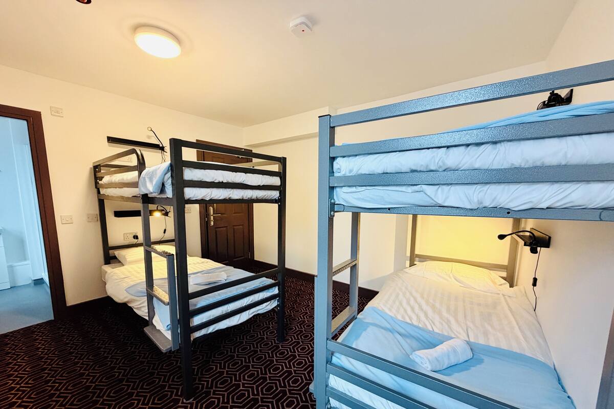 A room with two bunk beds, a door, a patterned carpet, and a light fixture.