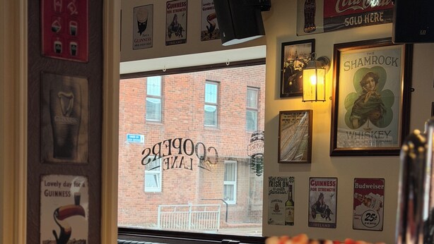 A restaurant interior with a brick wall, framed posters, and a window with a view of a building.