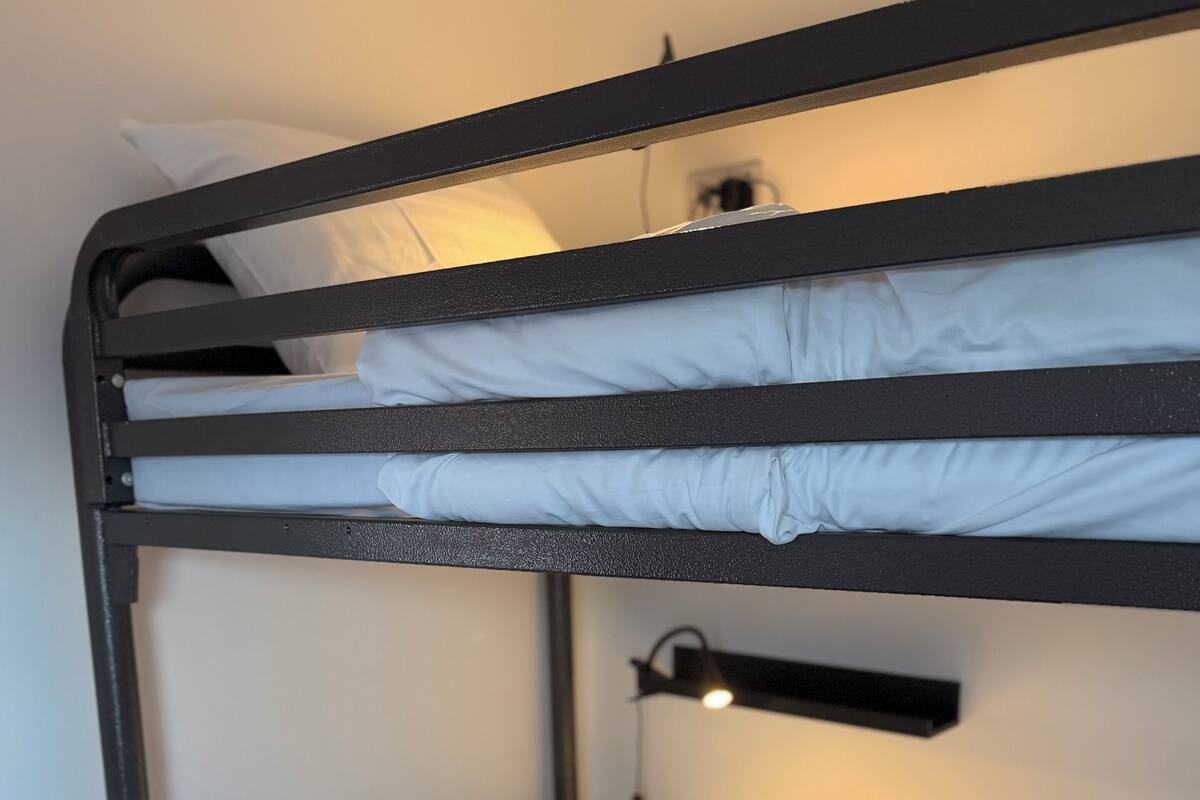 A bunk bed with white bedding and a bedside table with a lamp.