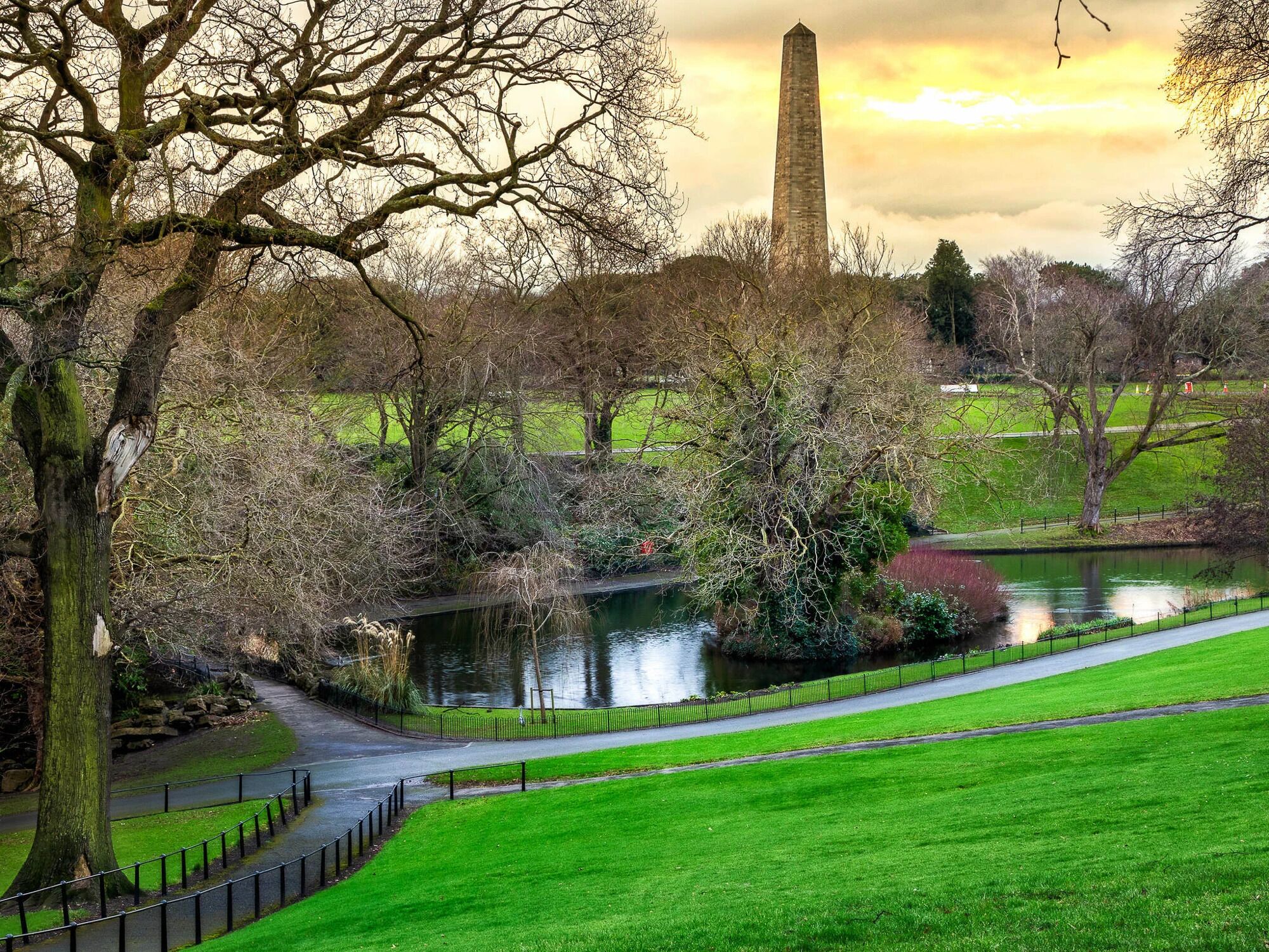 Un parque con un estanque, un sendero y un monumento alto.