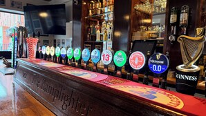 A bar with a row of beer taps, a Guinness tap, and a harp decoration.
