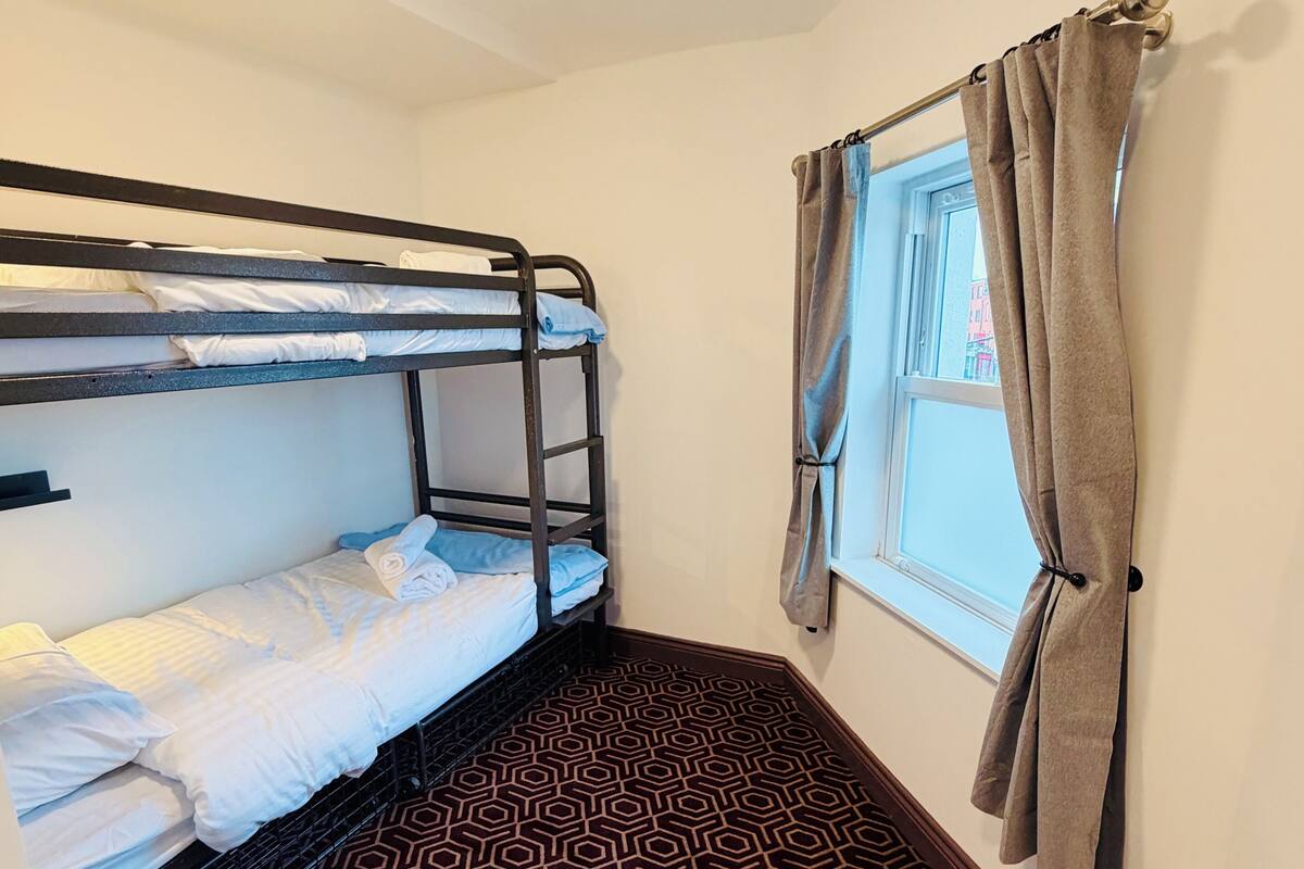 A bunk bed room with a geometric patterned carpet, a window with curtains, and a ceiling light.