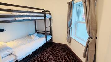 A bunk bed room with a geometric patterned carpet, a window with curtains, and a ceiling light.