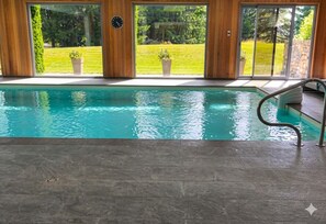 Una piscina interior con vistas a un jardín césped a través de amplios ventanales.