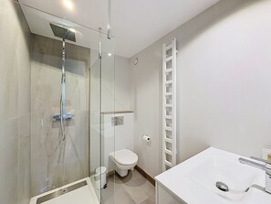 Een moderne badkamer met een douchecabine van glas, een toilet en een wastafel.