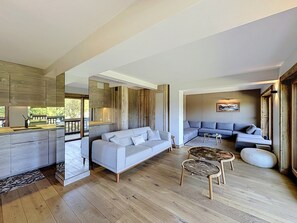 Un espacio habitable moderno con cocina, sofás grises, suelo de madera y una zona de comedor.