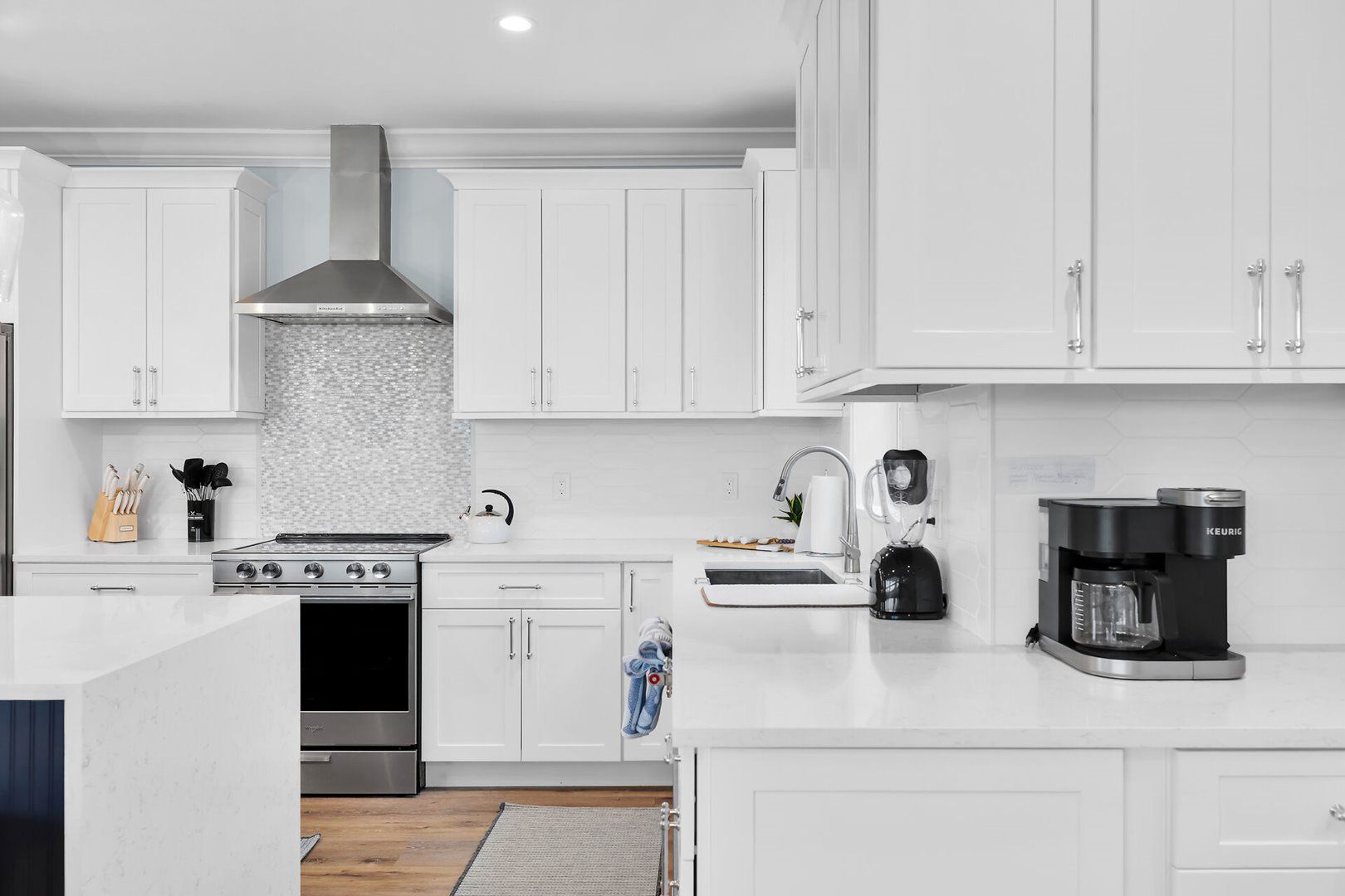 A modern kitchen with white cabinetry, a stainless steel range, a kettle, a coffee maker, and a tiled backsplash.