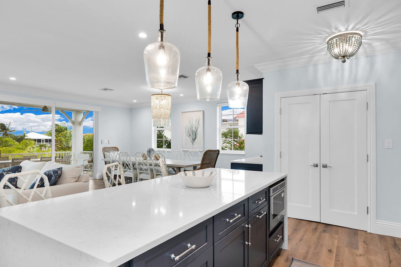 A modern kitchen with a large island, pendant lights, and a view of the outdoors.
