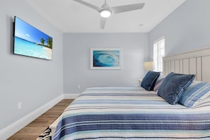 Ein Schlafzimmer mit einem Bett, einem Deckenventilator, einem Fernseher und einem gerahmten Bild an der Wand.